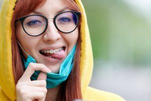 young woman with braces pulling down mask to smile 